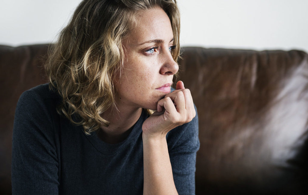 A person suffering from depression - female looking sidewise, thinking while sitting on brown leather couch against a white wall