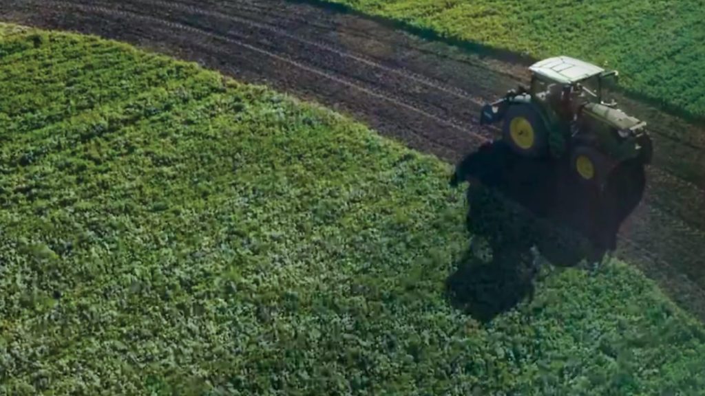 green tractor driving along dirt road through farmer field