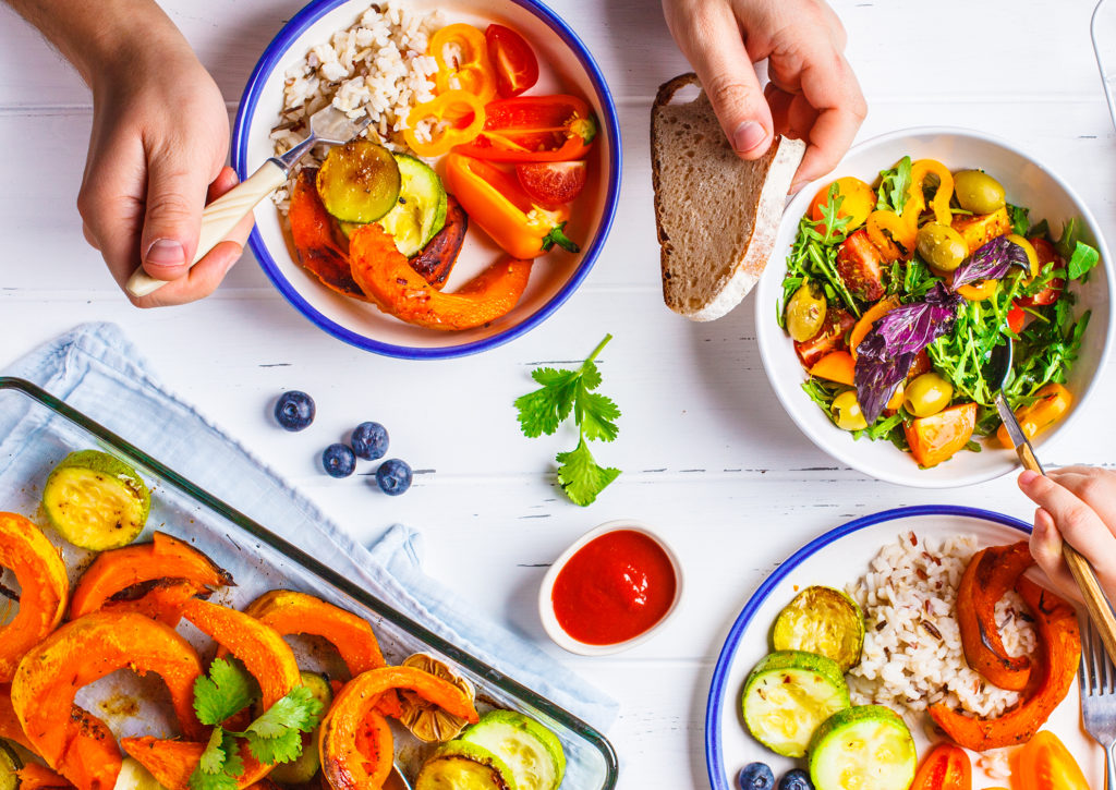 Flat lay of family hands eating healthy food. Vegan lunch table top view. Baked vegetables, fresh salad, berries, bread on a white background.