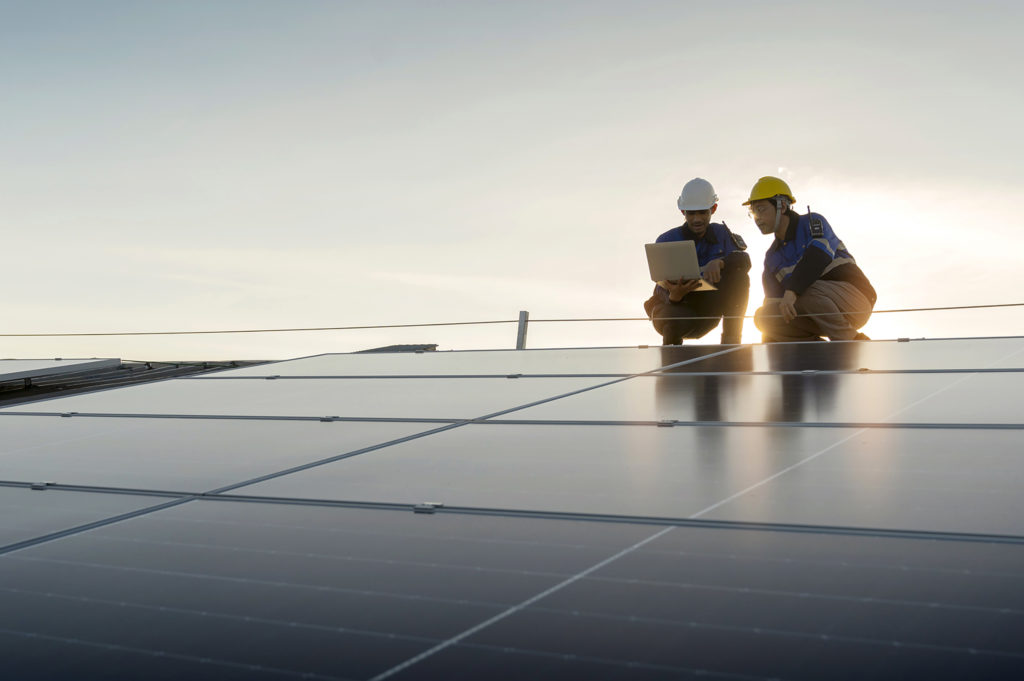 Specialist technician professional engineer with laptop and tablet maintenance checking installing solar roof panel on the factory rooftop under sunlight. Engineers team survey check solar panel roof.
