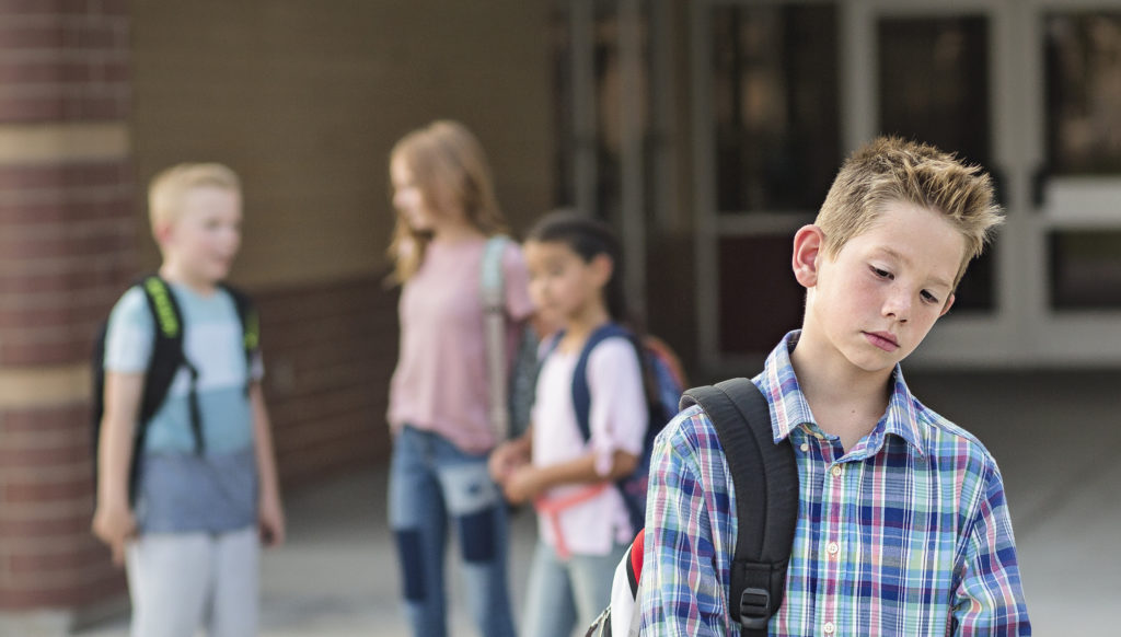 Sad boy feeling left out, teased and bullied by his classmates. Unhappy boy having problems fitting in with others at school