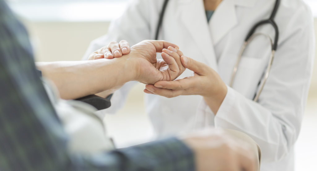Female doctor and senior man, checking pulse, holding patient's hand