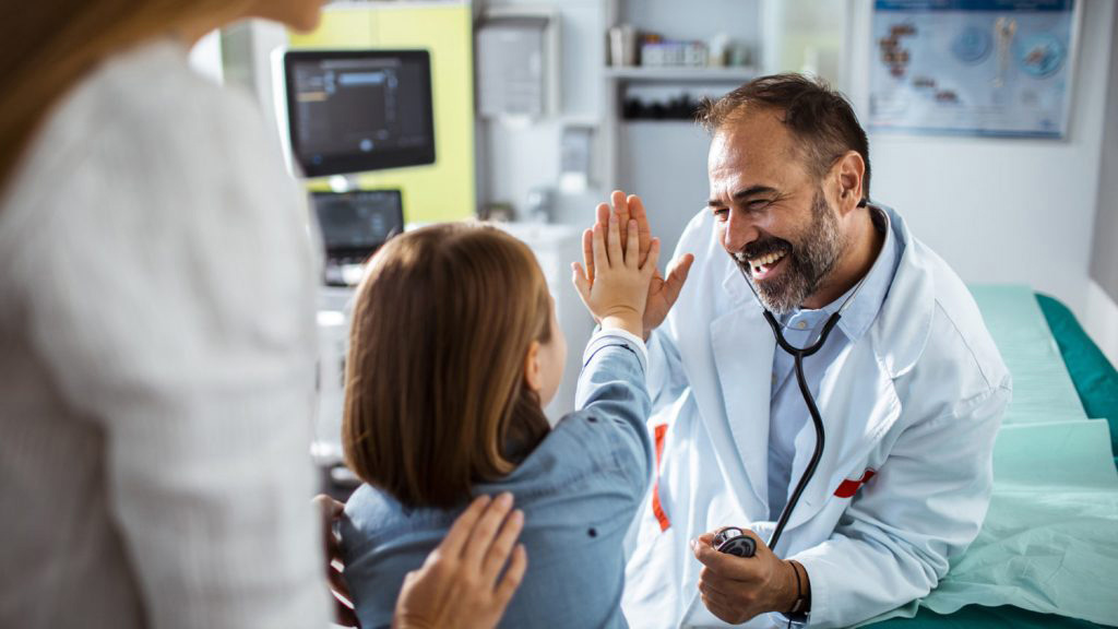male doctor doing a high five with child patient in hospital with back of mother to the side of the photo