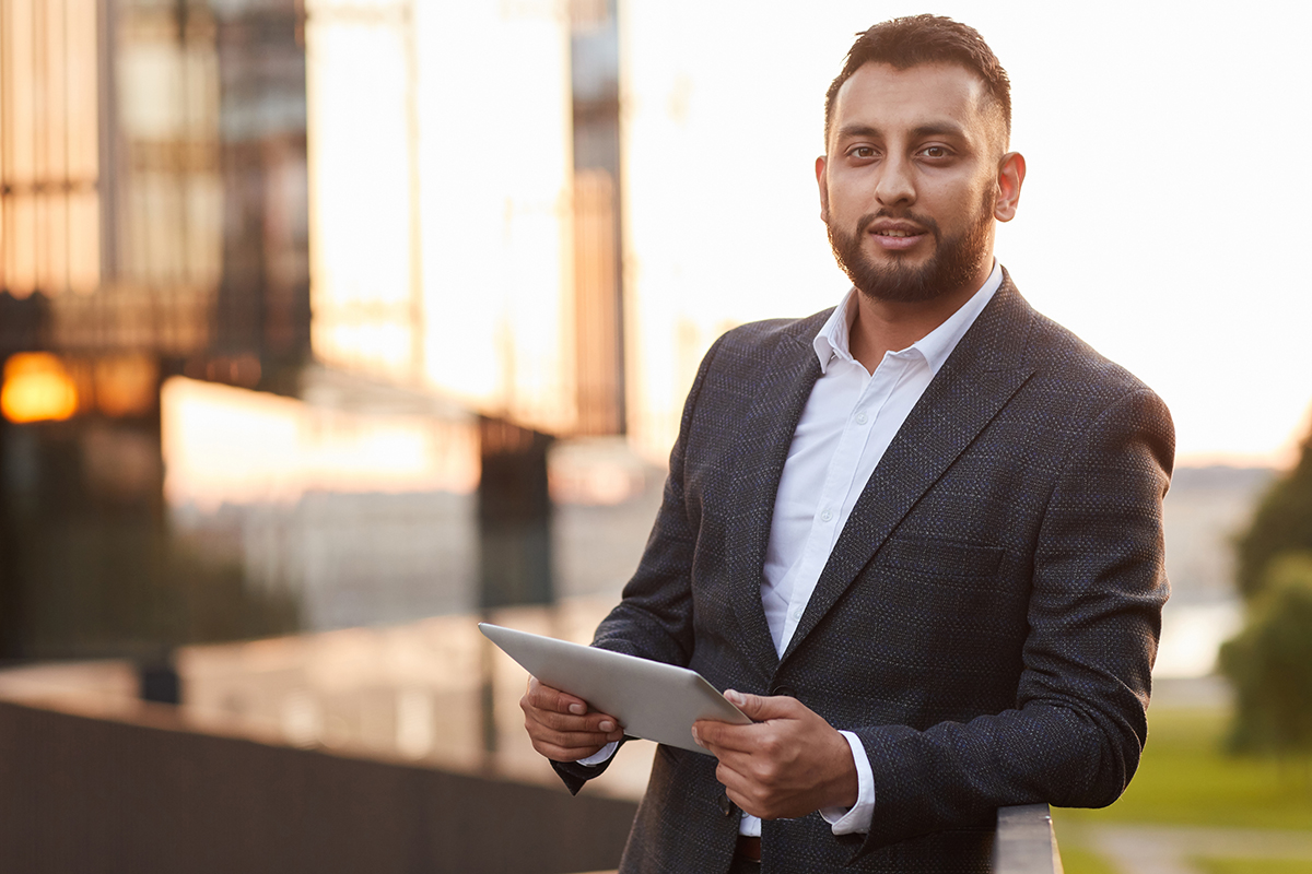 Portrait of young businesswoman in formal suit looking at camera while using digital tablet in the city