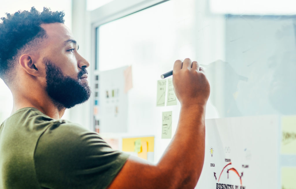 Shot of a young designer brainstorming with notes on a glass wall in an office