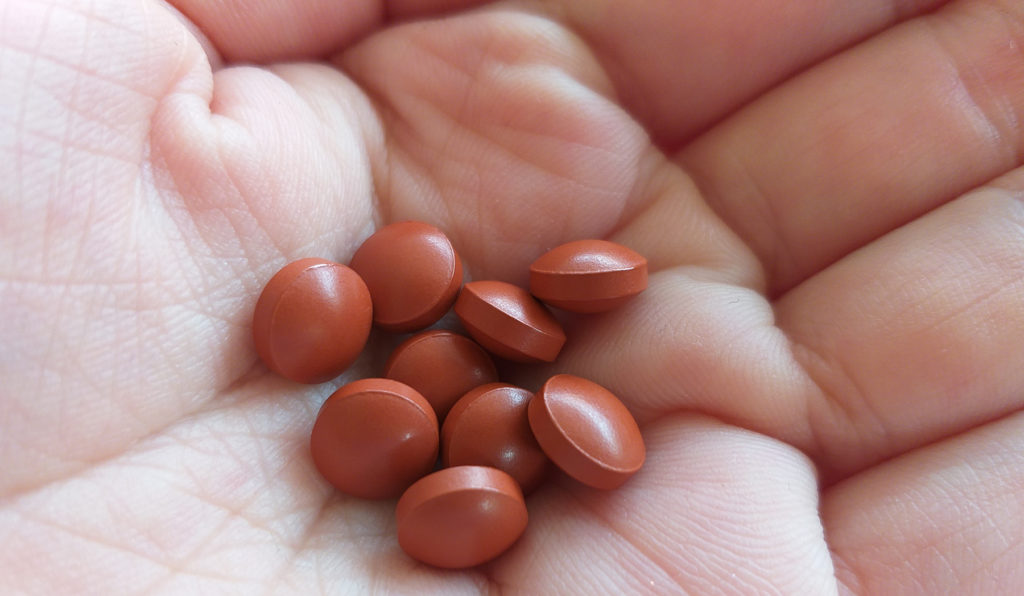 close up of hand holding nine orage pills, iron pills