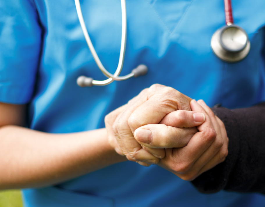 close up of nurse in blue scrubs with stethoscope holding older male hand, comforting